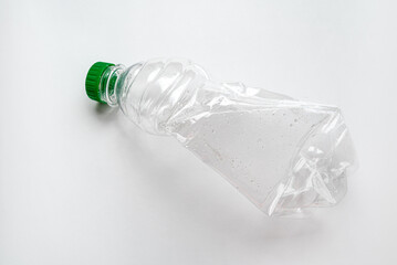 A crushed used plastic bottle with a green cap clean and prepared for recycling on a light background