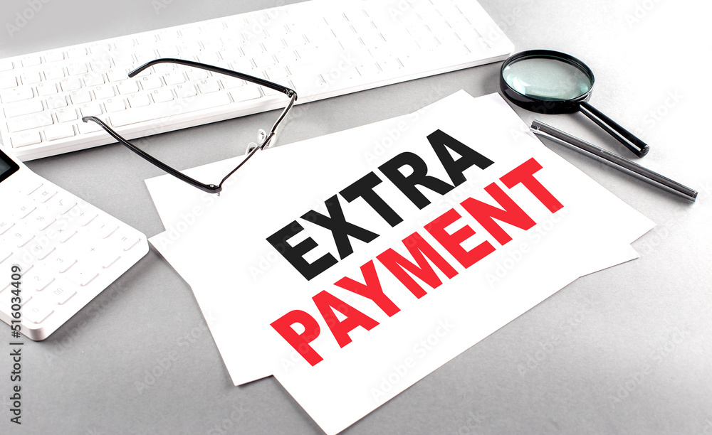 Poster extra payment text on a paper on a gray background near a calculator and a white keyboard