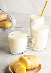 Glasses with vegan potato milk and potato tubers on concrete background. Selective focus.