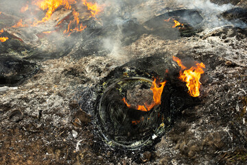 Burning wheels in landfill. Details of fire. Ashes and smoke.