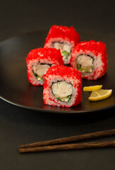 Sushi (rolls) serving on a black plate, black background
