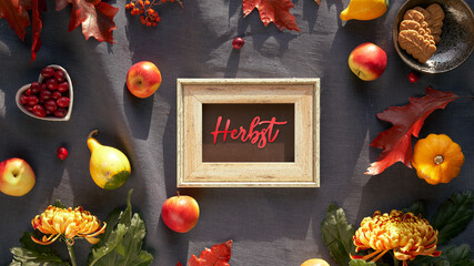 Text Herbst means Autumn in German language. Blackboard, frame and Autumn decor. Chrysanthemum flowers, bunny tail grass and red oak leaves, pumpkins, cranberry. Fall decor, flat lay on dark textile.