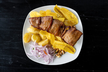 Typical food of the Peruvian: Cecina with potatoes, crispy banana chips and onion. Top view