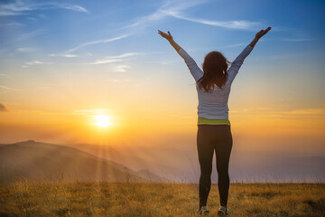 Young happy woman jumping at sunset mountains with sunset hills and mountain landscape