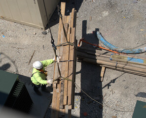 Chicago, Illinois, USA. June 28, 2022. Looking down on a construction worker who is operating a remote controled crane to move a bundle of lumber.