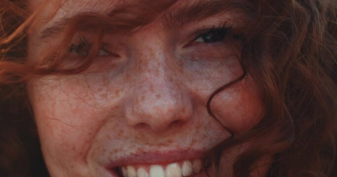 Face sunshine young smiling woman with red curly hair look at camera in the city streets at sunlight. Happy portrait. Slow motion