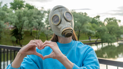 A girl in a gas mask with her hands shows a heart symbol. Alienation in the city. Fashion, ecology...