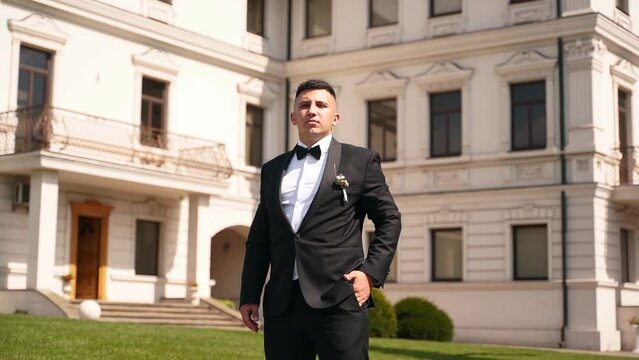Bossy rich man in a suit and bow tie sits on leather sofa drinking glass of whiskey. Confident imperious groom posing on wedding day.