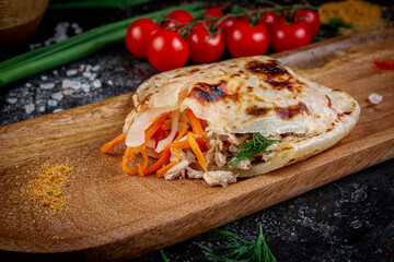 Pita with grilled chicken and vegetables with sauce in a pita on a dark stone table. Fast food restaurant, delivery service.