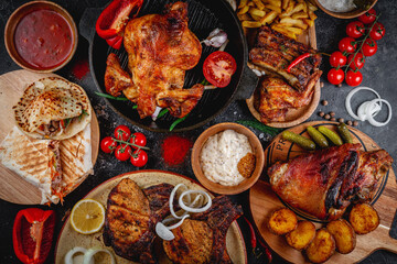 An assortment of grilled meat dishes on the table. Grilled chicken, beef ribs, shawarma, pork ham, French fries and creamy with tomato sauce. Fast food restaurant, delivery service. Top view, flatlay.