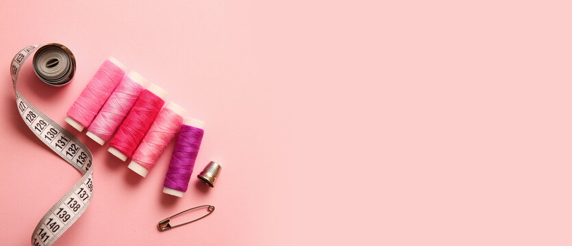 Colorful sewing threads and measuring tape on pink background with space for text