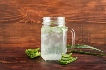 Glass jar of aloe juice with leaves on wooden background