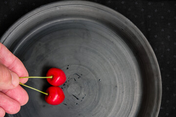 Fototapeta na wymiar A hand puts a cherry on a plate. Red cherries on a black ceramic plate. Copy space. 