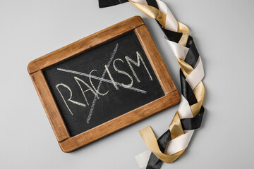 Chalkboard with crossed out word RACISM and braided ribbons on grey background