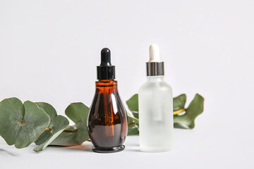Bottles of natural serum and eucalyptus branch on white background