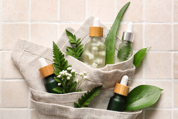 Composition with bottles of serum, plant leaves and napkin on light tile, closeup