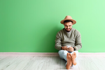 Handsome barefoot man using mobile phone near green wall