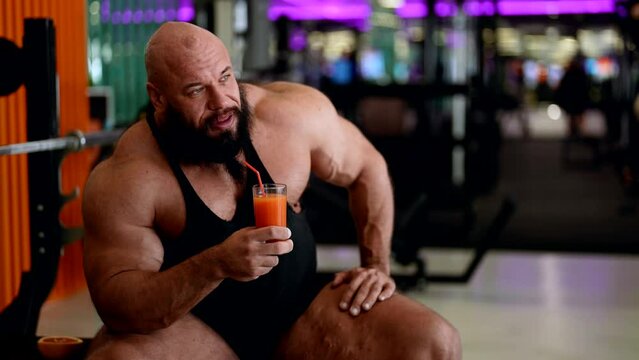 sporty man with large muscles is resting in gym and drinking vitamin juice cocktail, powerlifter