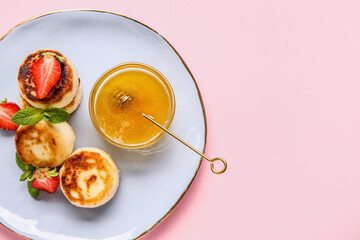 Plate with cottage cheese pancakes, strawberry and honey on pink background