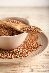 Plates and spoon with buckwheat grains on light wooden background, closeup