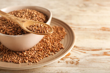 Plates and spoon with buckwheat grains on light wooden background, closeup