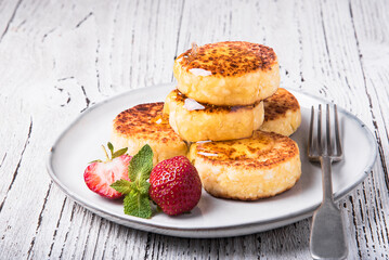 Obraz na płótnie Canvas Cheesecakes with strawberries and honey on a white table.