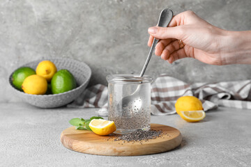 Woman stirring chia seeds in glass of water on grey background