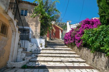 Fototapeta na wymiar Stone steps leading to old colorful houses with pink plant on the right in Corfu Greece