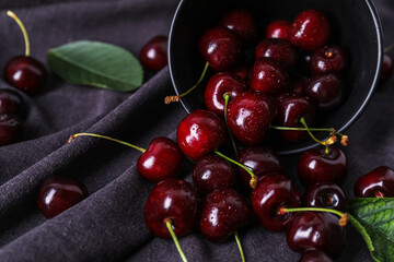 Overturned bowl of ripe cherries on fabric background, closeup