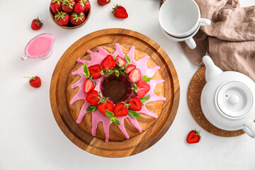 Wooden board with tasty strawberry cake, cups and teapot on light background