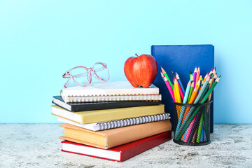 School stationery with apple and eyeglasses on table against blue background