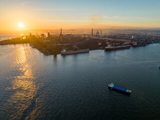 Cargo ships docked at large industrial facility with smokestacks at sunset - 516049650