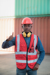 African black male worker standing, great thumbs up  and wearing safety work equipment clothes Work at a warehouse of Overseas shipping port, ship, cargo, import-export  industry.