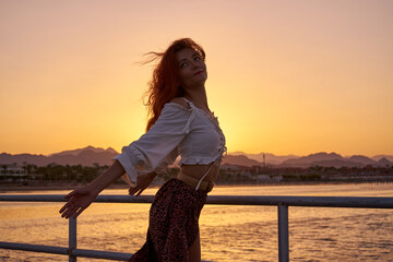 Back view of travel  woman with long hair on sea beach at sunset in summer with mountain and Red sea background.eauty woman silhouette at sunset with long healthy wet hair enjoying nature background 