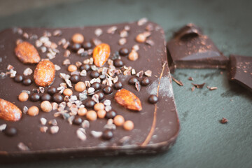 Chopped dark chocolate with almond and coffee beans. Broken chocolate on black plate. Sweet food. Dark chocolate with nuts. Coffee product. 
