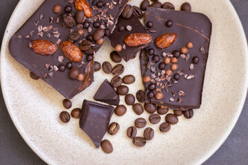 Chopped dark chocolate with almond and coffee beans. Broken chocolate on beige plate. Sweet food. Dark chocolate iwith nuts. Coffee product. 