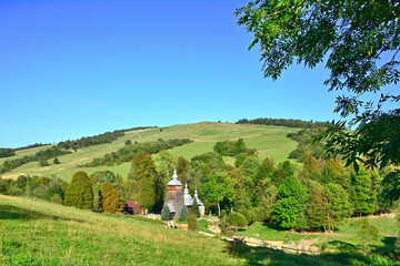 Rural landscape in Low Beskids (Beskid Niski) with wooden orthodox church in Chyrowa village, Poland.  - obrazy, fototapety, plakaty