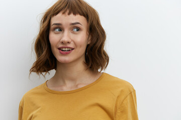 a beautiful, sweet, relaxed woman stands on a light background in a yellow T-shirt and looks away with a pleasant smile. Horizontal photo with an empty space for inserting an advertising layout