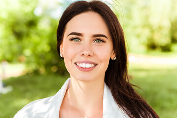 Close up head portrait of smiling caucasian woman with white teeth looking at the camera. Perfect healthy smile with veneer. Skin and dental care. Nature green background.
