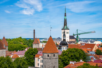 Scenic view of gothic church amidst red roof houses. Viewpoint of old historic townscape in Tallinn. Beautiful scenery of medieval capital city with high towers against blue sky.