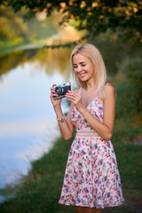 pretty blondy woman holds a camera and smiles near a river