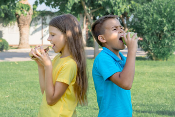Schoolchildren eat hamburgers in the park.