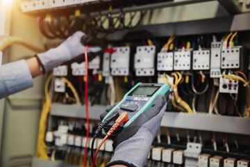 Electricity and electrical maintenance service, Engineer hand holding AC multimeter checking electric current voltage at circuit breaker terminal and cable wiring main power distribution board.