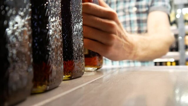 Close-up of glass bottles with liquor or cognac and a male buyer takes one