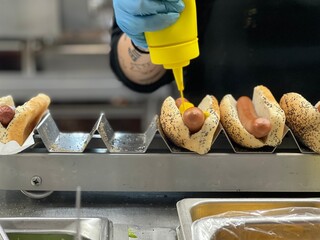 mustard being squeezed onto hot dogs being prepared to serve