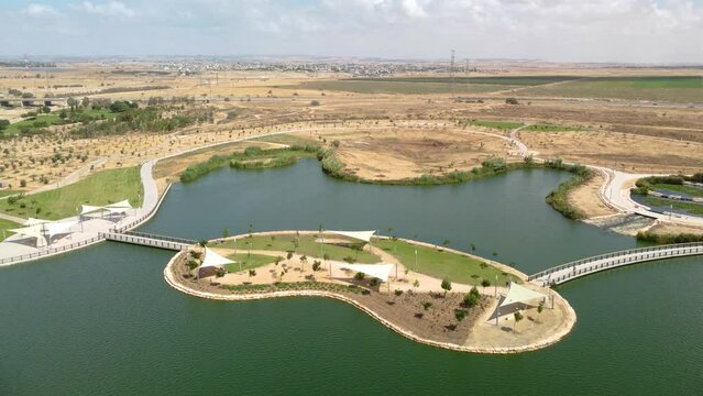 Flying over the small island on artificial lake in the park with Beer Sheva buildings at background