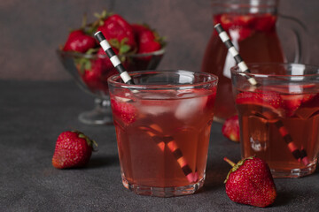 Cold strawberry compote in two glasses with drinking straws and also a jug on brown background