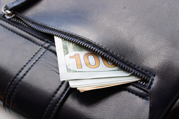 dollars are sticking out of a leather bag with an unbuttoned zipper