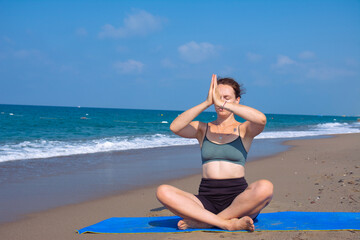 Fototapeta na wymiar A beautiful girl is doing yoga on the beach near the sea