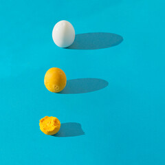 Egg white and whole and semi eaten yolk in row with long shadow on blue background. Square composition with copy space. Healthy breakfast concept.